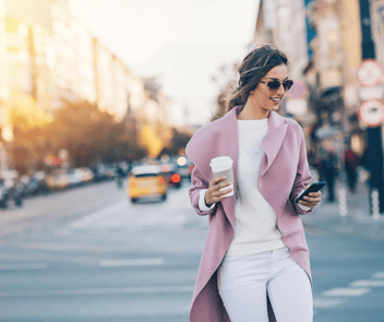 Woman walking and texting with coffee in city